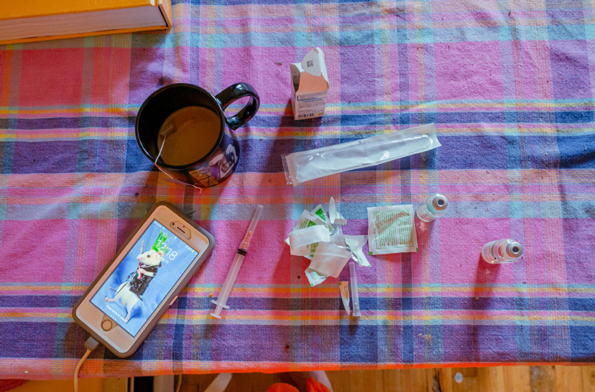 Photographie issue de la série Puberty de l'artiste : on voit une aiguille avec de la testostérone, un cellulaire et un café sur une table colorée.